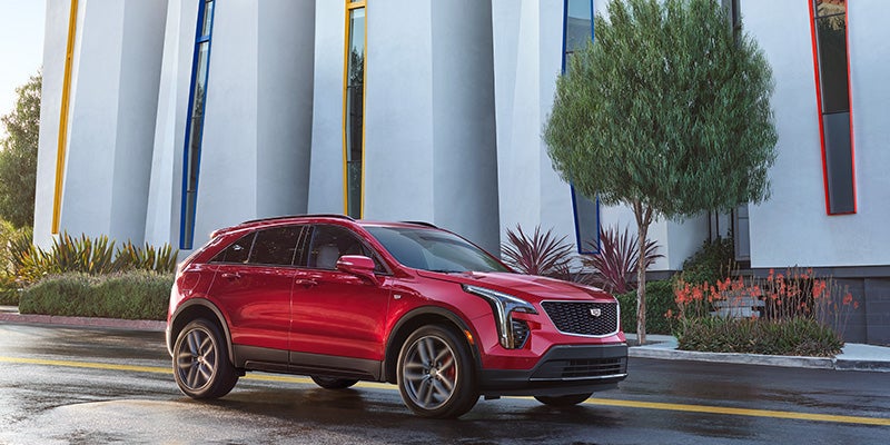 Red Cadillac XT4 parked on a modern city street in front of a stylish building with tall windows and colorful accents.