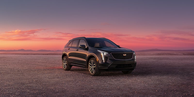 Black Cadillac XT4 parked in a wide open desert landscape during sunset, with a pink and purple sky in the background.