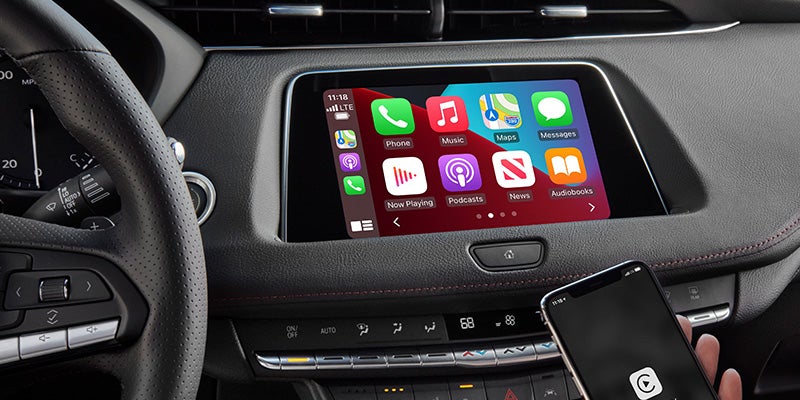 Close-up of the Cadillac XT4's dashboard showing the infotainment system with Apple CarPlay and a hand holding a smartphone.
