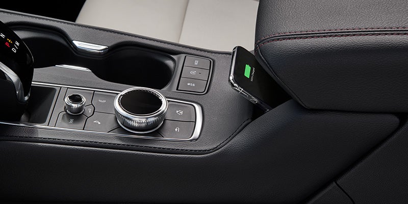 Close-up view of the Cadillac XT4's center console featuring control dials, drive mode selector, and a smartphone wirelessly charging beside the armrest.