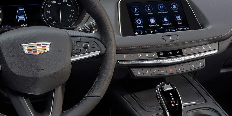 Interior view of the Cadillac XT4 showing the digital infotainment system and surrounding dashboard controls, with a focus on the steering wheel and gear shifter.