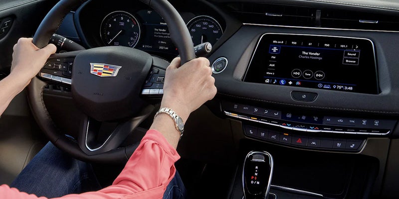 Person driving a Cadillac XT4, interacting with the multimedia touchscreen display while holding the steering wheel.
