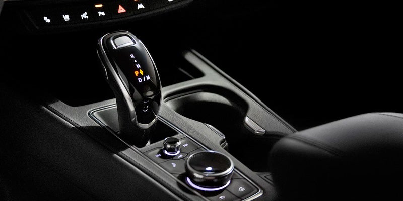 Close-up of the Cadillac XT4's electronic gear shifter and rotary control knob on the center console, illuminated in low light.