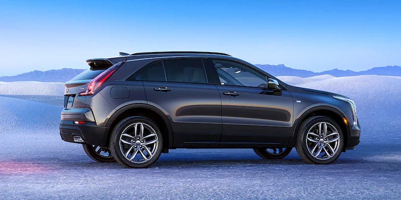 Side view of a black Cadillac XT4 parked on a snow-covered landscape under a clear blue sky, with mountains in the distance.