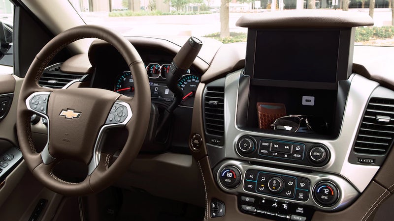 Interior view of a Chevrolet Tahoe, focusing on the steering wheel with the Chevrolet logo, dashboard, and raised infotainment screen.