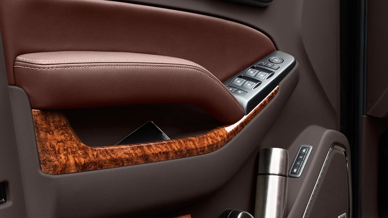 Close-up of a Chevrolet SUV’s interior door panel, featuring leather trim, wood accents, and window and lock controls.
