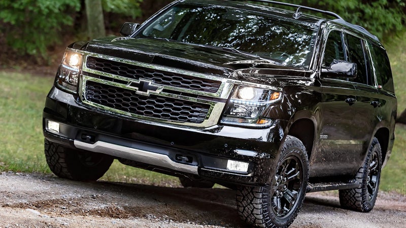 A black Chevrolet SUV driving on a rugged, muddy path in a forested area, highlighting its off-road capability and rugged design.