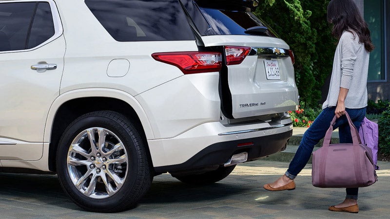Rear view of a white Chevrolet Traverse with a woman using the hands-free power liftgate, carrying a purple bag.