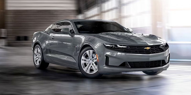 Gray Chevrolet Camaro sports car in motion inside a modern industrial garage setting.