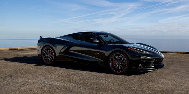 A sleek black Chevrolet Corvette parked on a seaside road with a clear blue sky and ocean in the background.