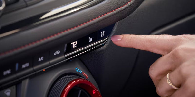 Close-up of a hand pressing the heated seat button on the 2025 Chevrolet Blazer’s climate control panel with red stitching detail.